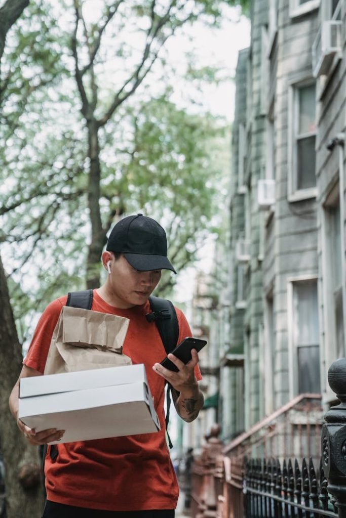 Courier wearing a red shirt, using smartphone while delivering packages in an urban street.